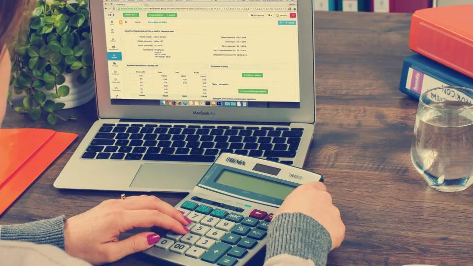Mãos usando calculadora ao lado de um notebook com planilha de despesas