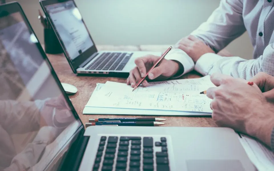 Pessoas revisando documentos e anotações ao lado de notebooks