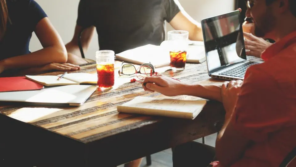 Equipe reunida em mesa de trabalho com papéis, notebook e anotações